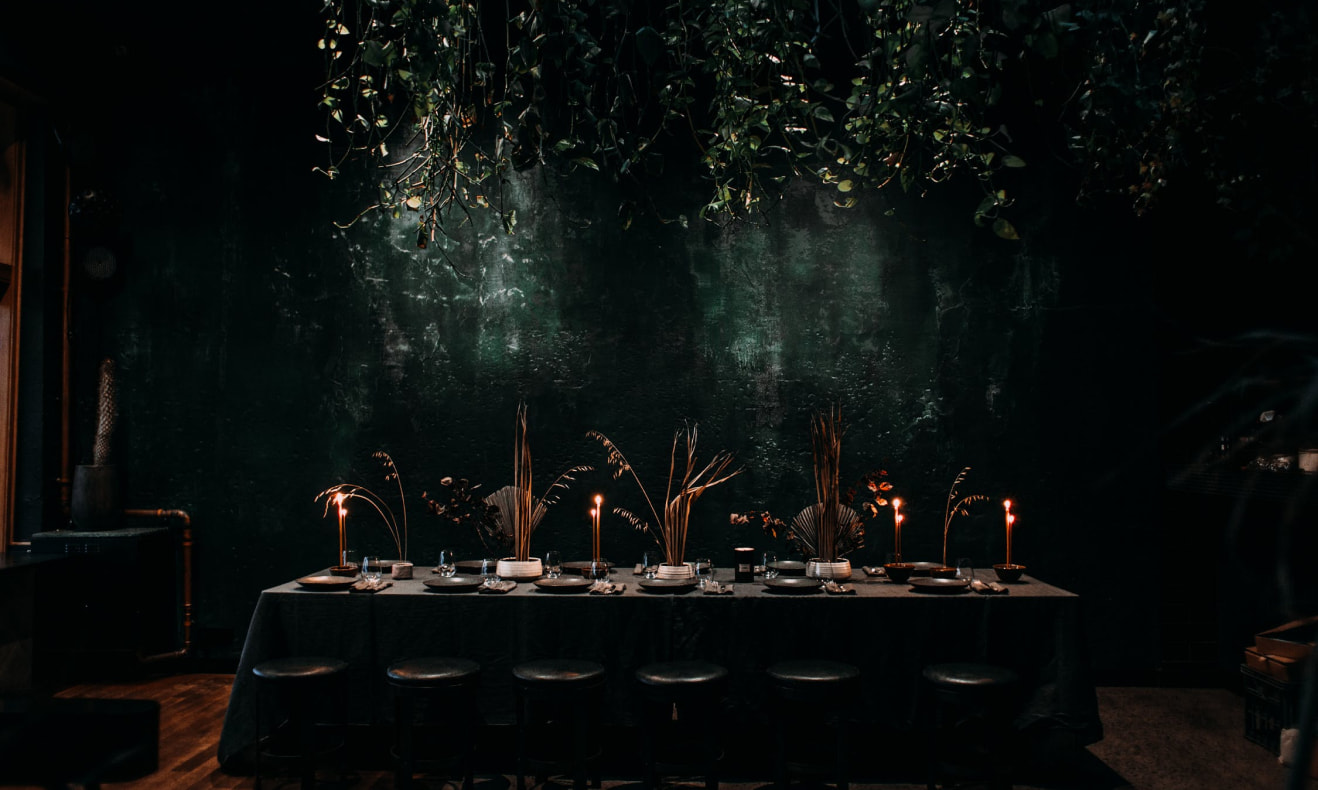 A long candlelit dinner table set beneath hanging foliage